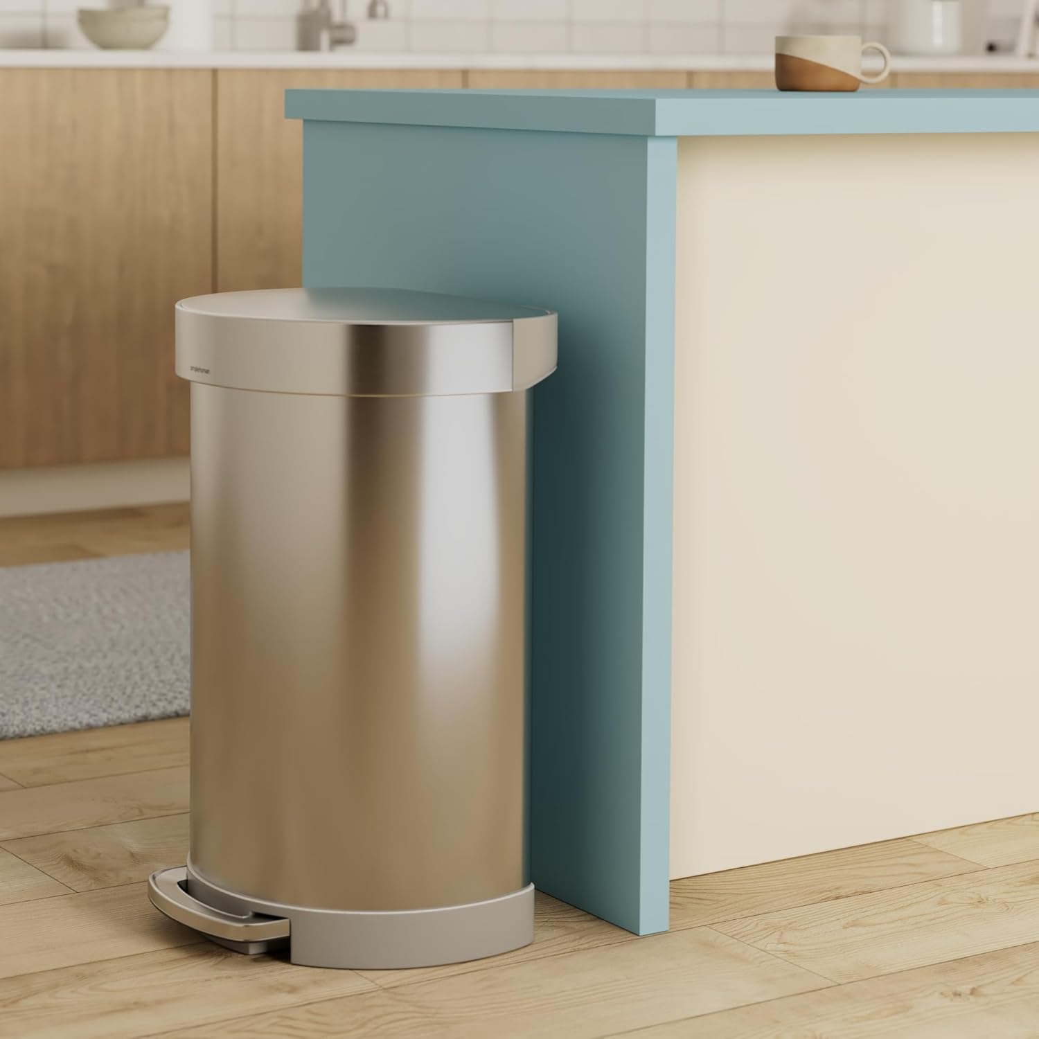 Brushed stainless steel semi-round step trash can with metal pedal and silent-close lid, shown in modern kitchen setting — side