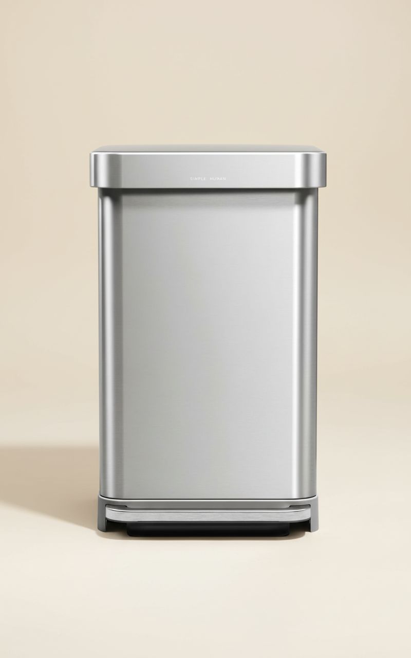 Rectangular brushed stainless steel step trash can with grey plastic lid and pedal mechanism, shown in modern kitchen setting — hero view 1